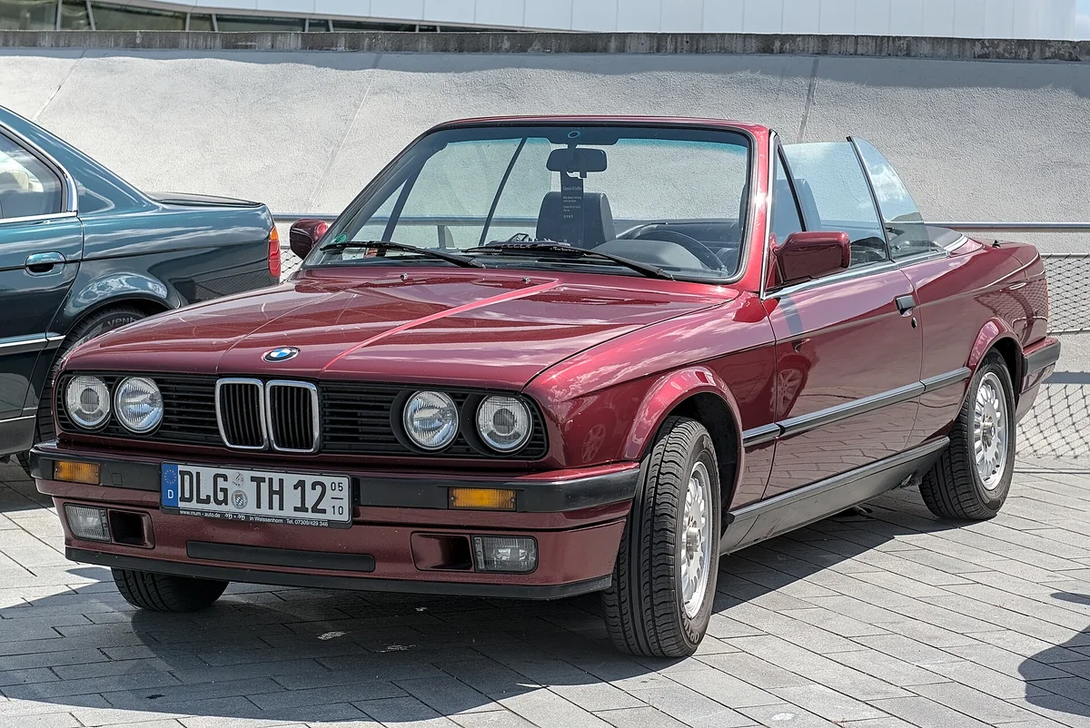 A red BMW E30 3 Series convertible with the roof down