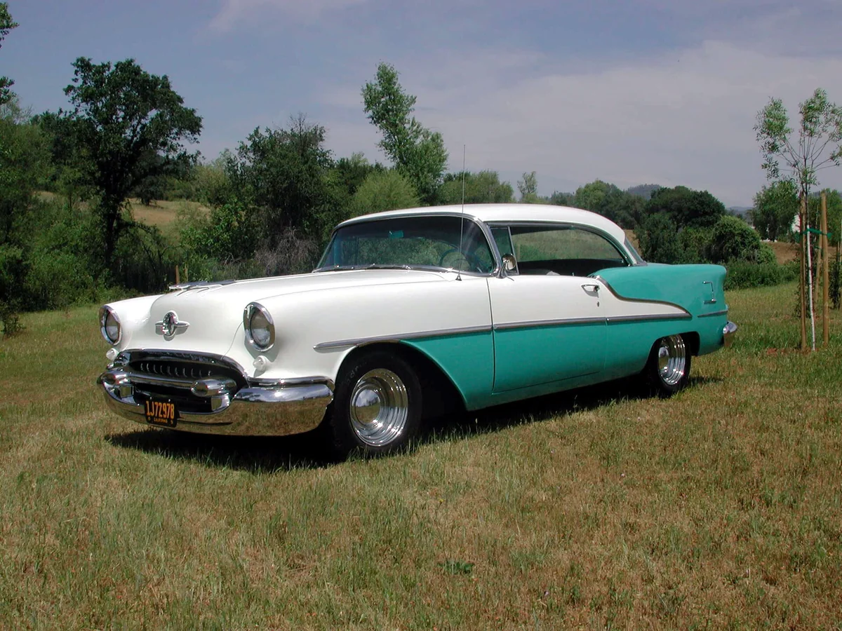 A teal and white 1955 Oldsmobile 88 parked on grass